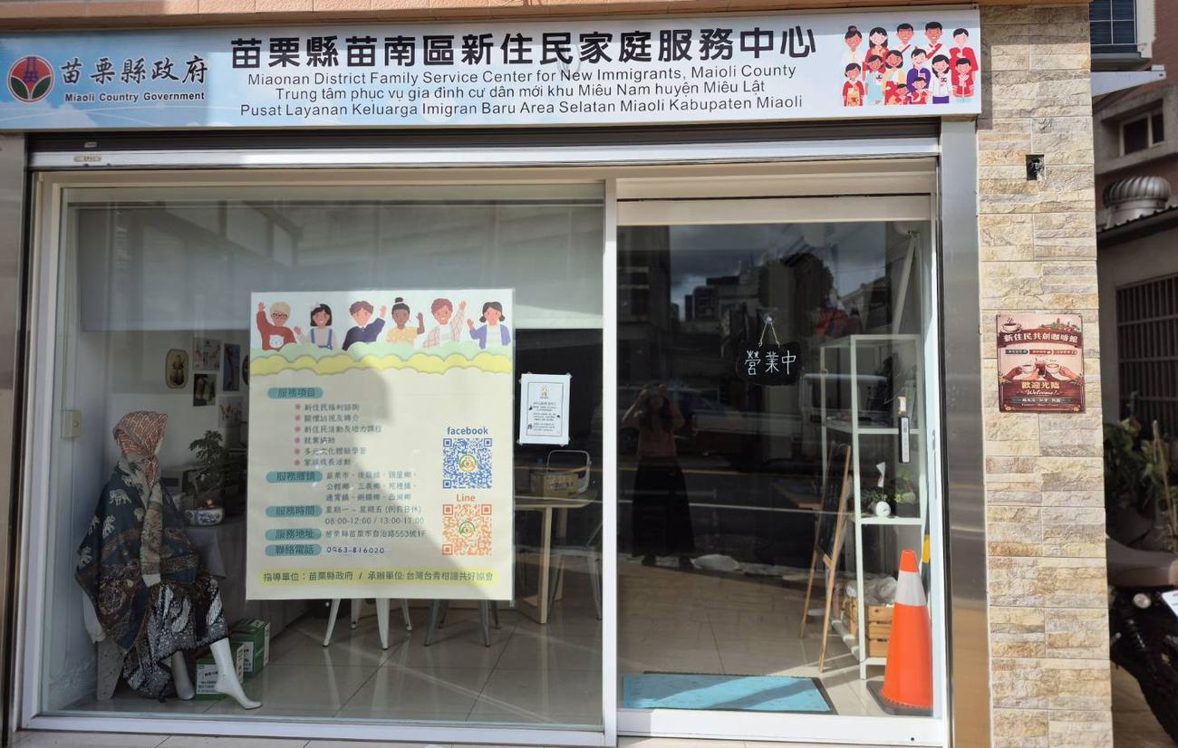 苗栗縣苗南區新住民家庭服務中心的店門口，招牌上有中文、英文、越南文和印尼文，玻璃門上掛著營業中的牌子